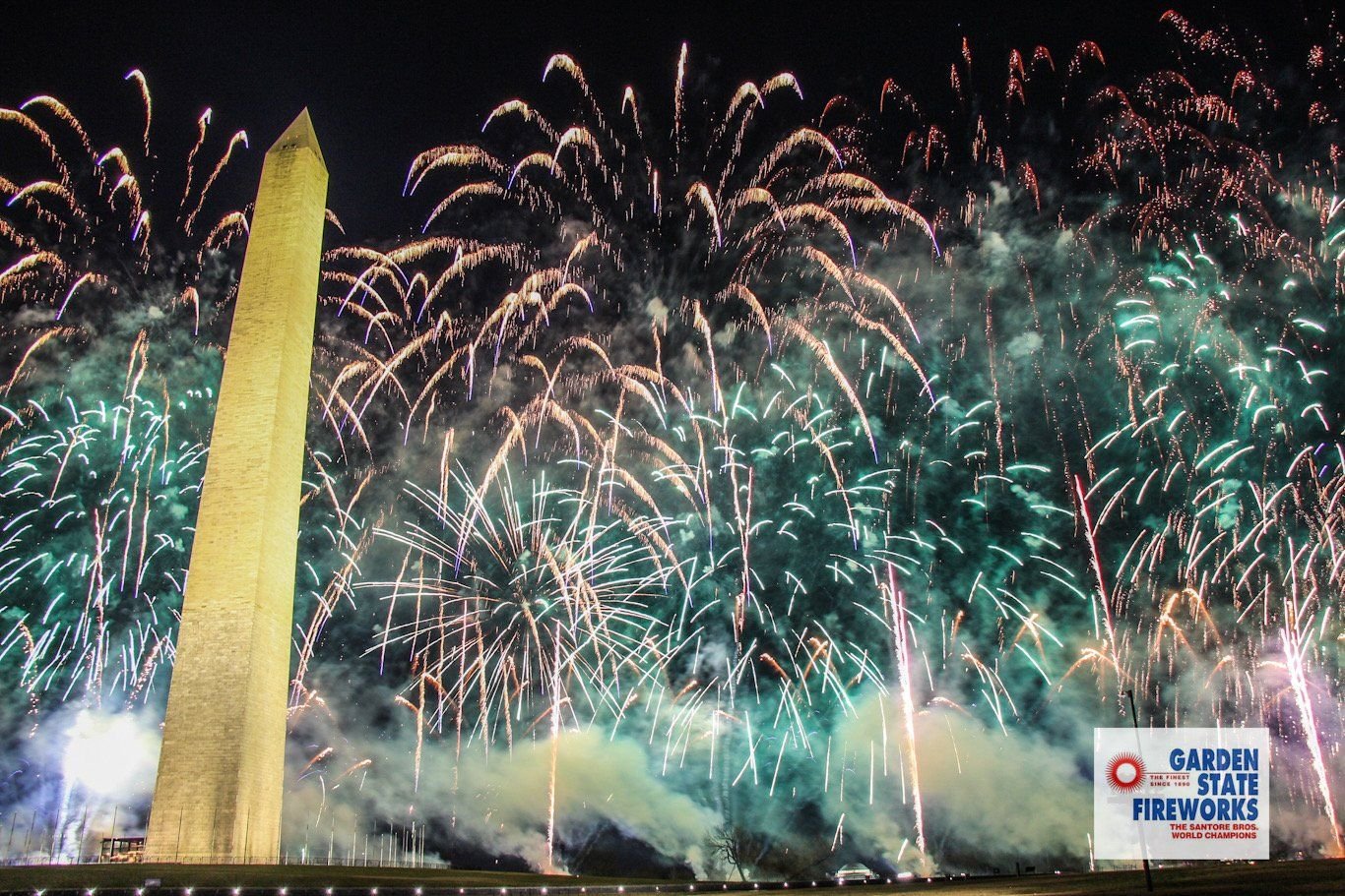 Teal, gold and white fireworks bursting beside the Washington Monument at night during the 2021 inauguration show