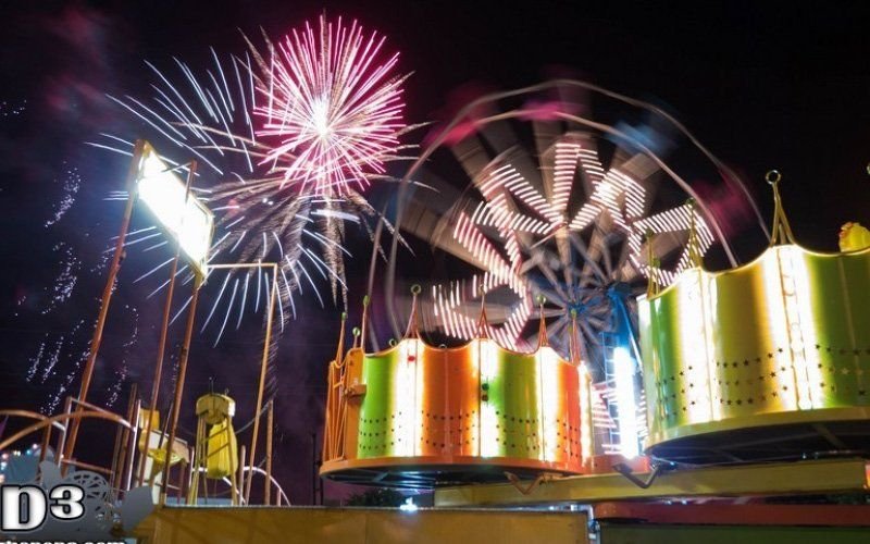 Pink and white firework burst above brightly lit spinning carnival rides at night