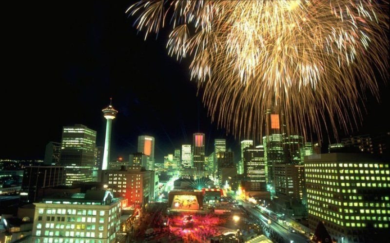 Large gold fireworks bursting over the lit downtown skyline and tower of Calgary at night