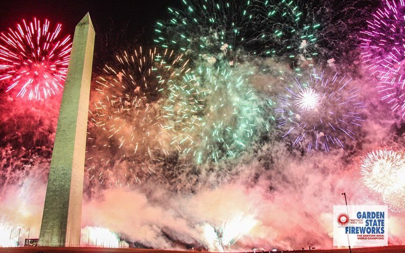 Red, green, purple and gold fireworks and smoke beside the Washington Monument at night