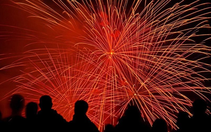 Orange firework burst filling the night sky above a crowd of silhouetted spectators