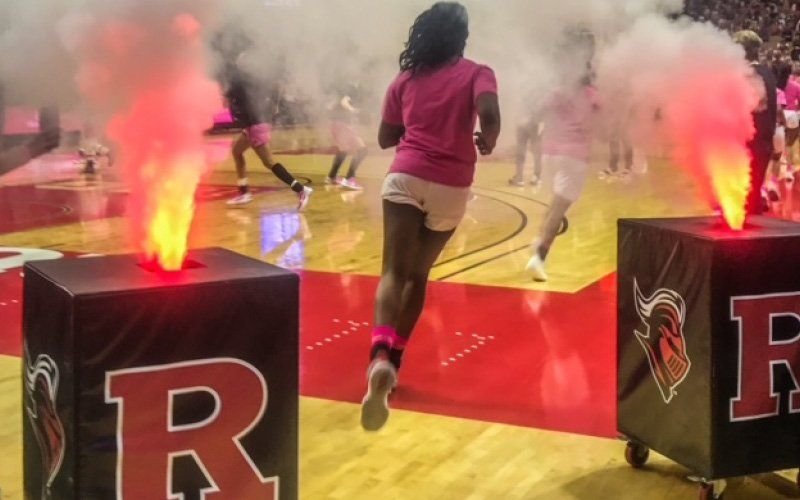 Basketball players running onto a court between two cabinets venting fire and smoke at a college arena