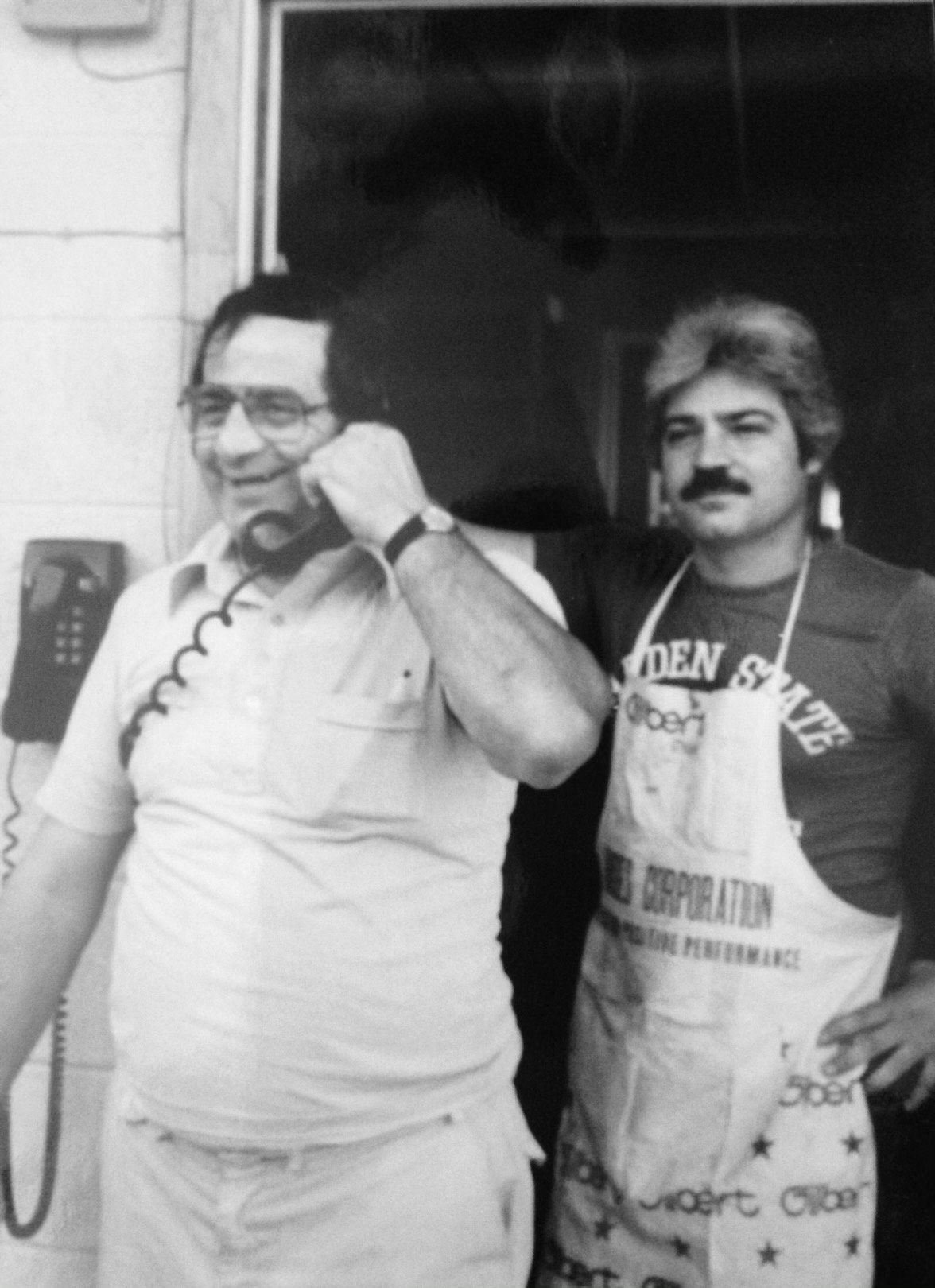 Archival black-and-white print of Dominick Stallone and Nunzio Santore in the press room, one on a wall phone