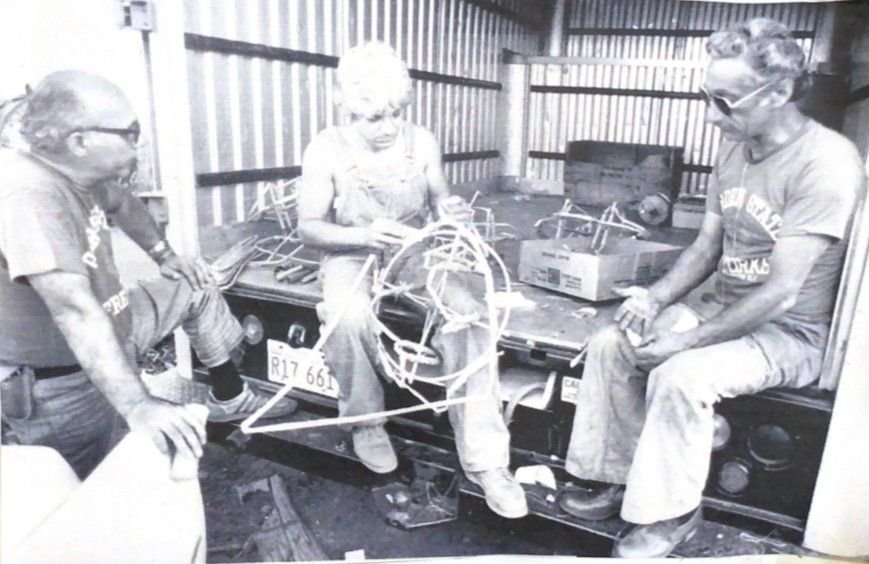Three men sitting on a truck bed building wire set pieces for the 1980 Macy’s July 4th show