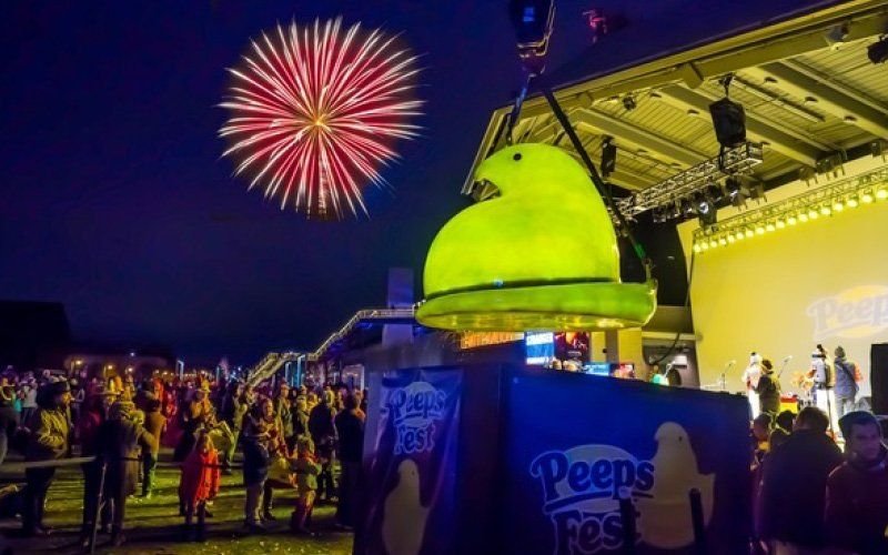 Red and white firework above a crowd at Peeps Fest, with a giant glowing green Peeps chick on stage